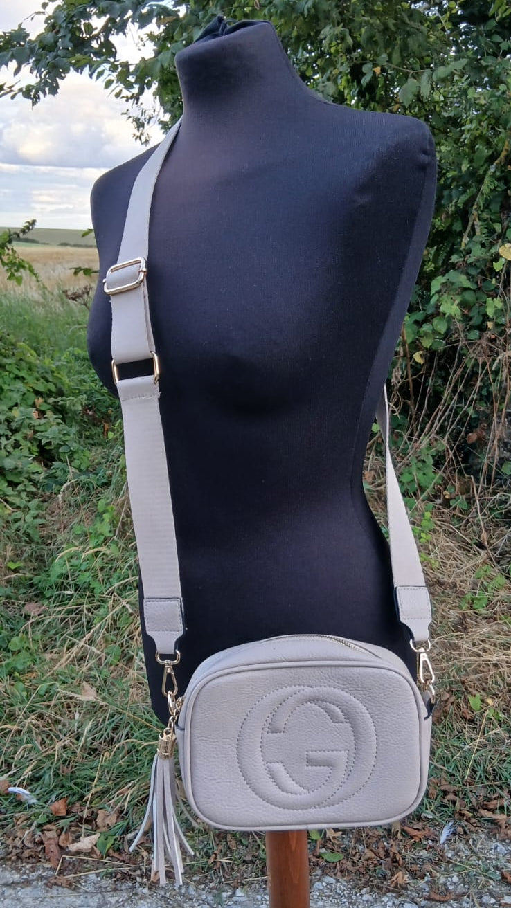A white Gucci crossbody bag with a tassel and embossed GG logo.